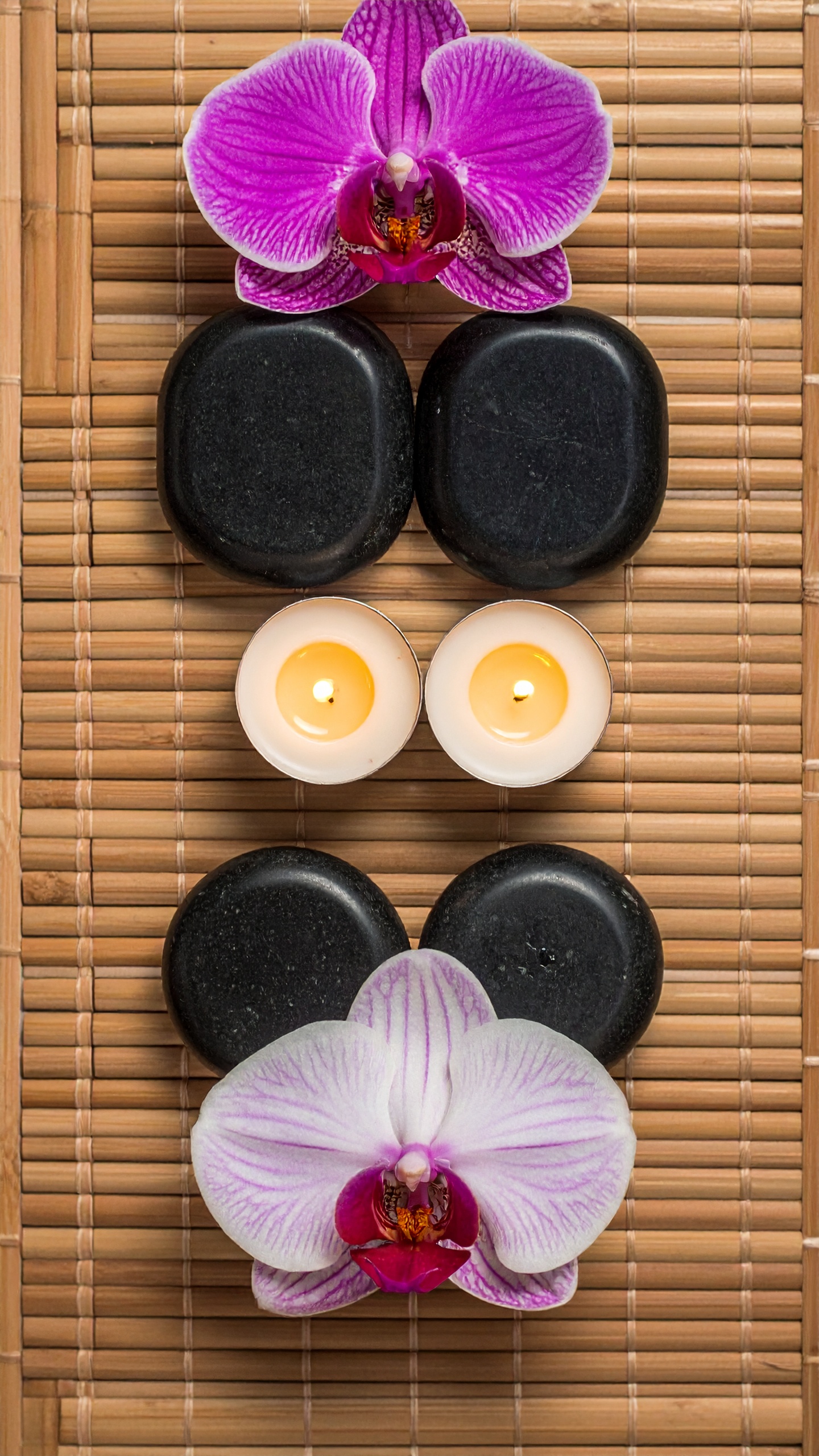 Elegant spa setup with orchids, candles, and stones on bamboo mat