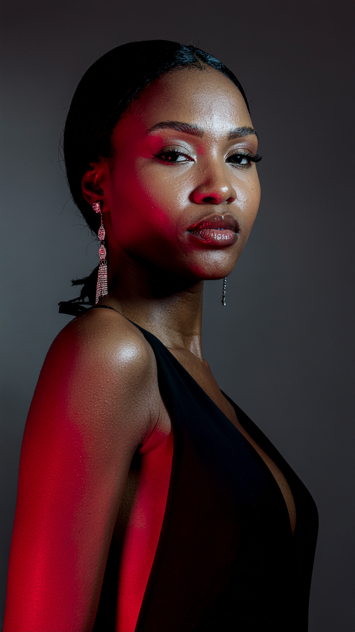 Elegant woman in a sleek black dress, highlighted by red lighting