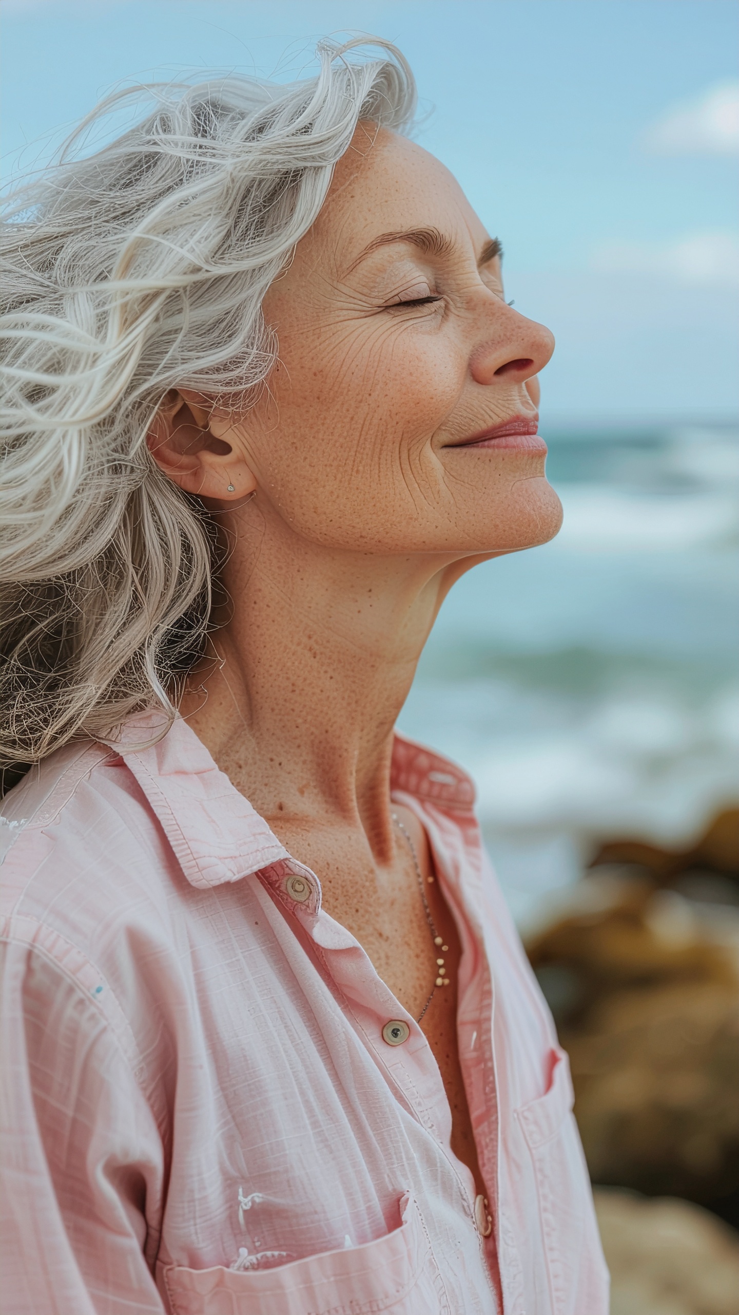 A serene older woman enjoys the ocean breeze, embodying tranquility and confidence