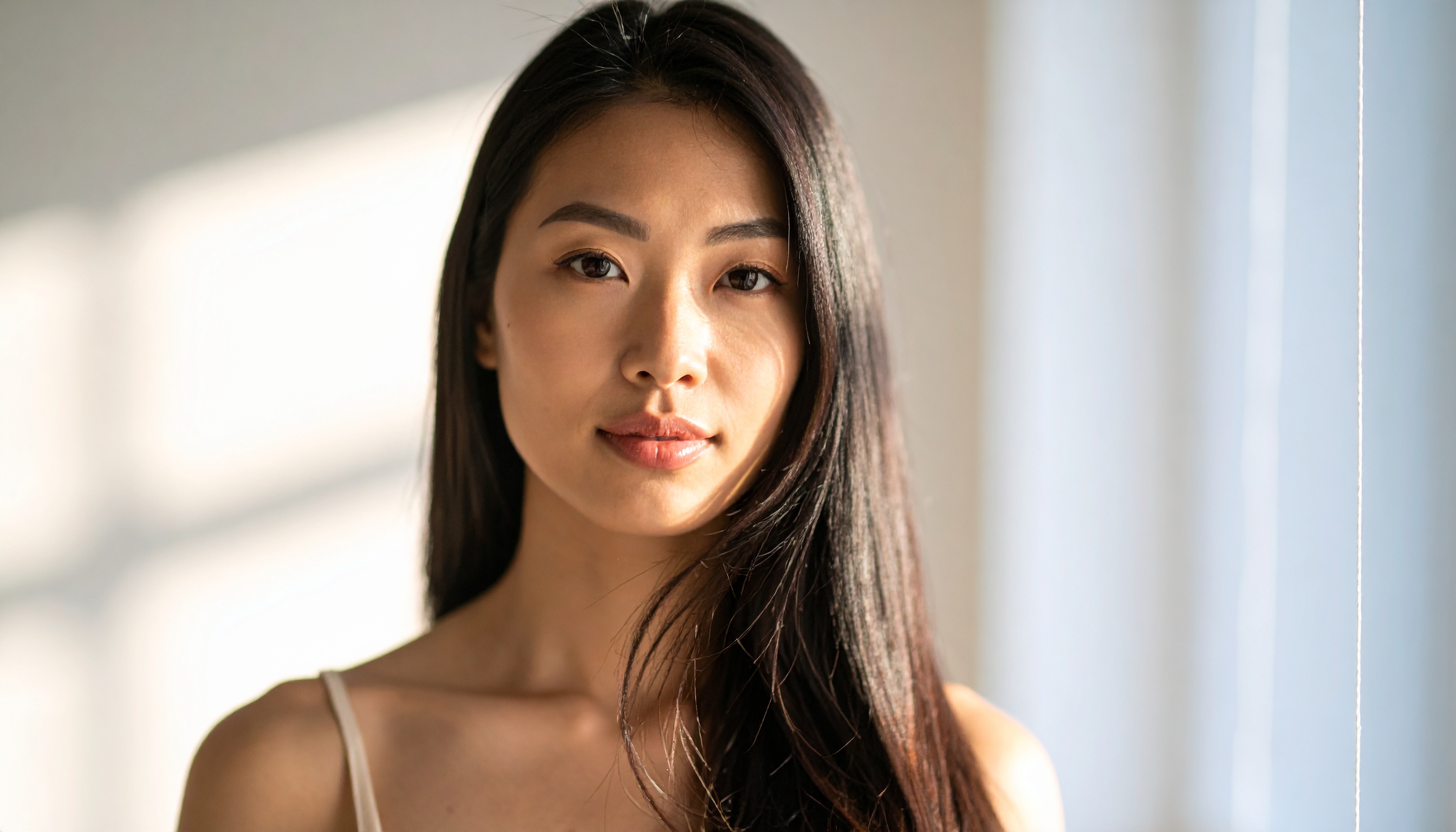 A woman with long, dark hair is illuminated by soft natural light