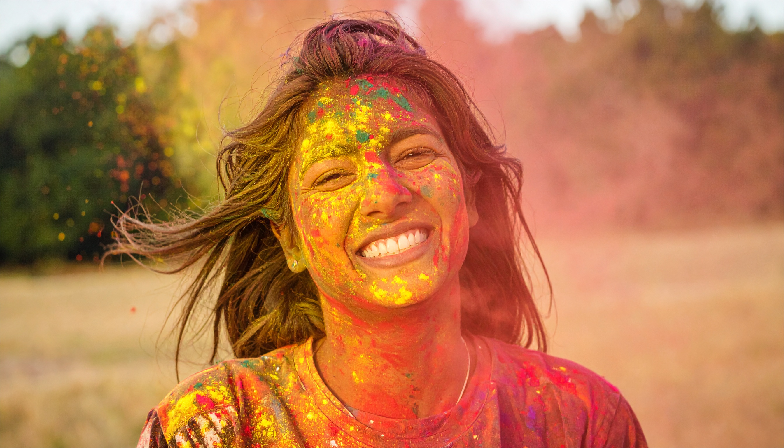 A joyful person covered in vibrant Holi colors smiles brightly outdoors