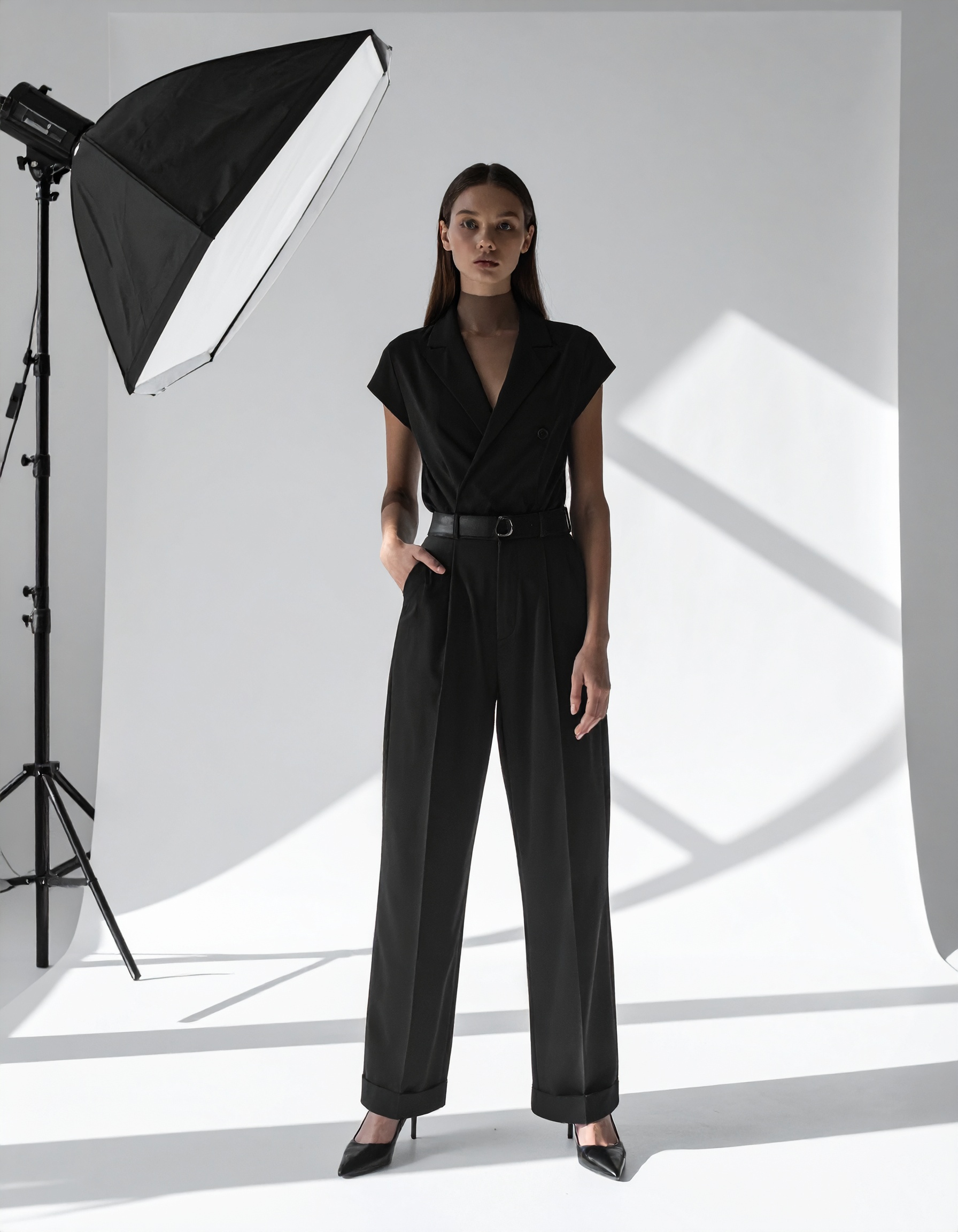 A woman stands confidently in a professional photo studio setting wearing a sleek, tailored black