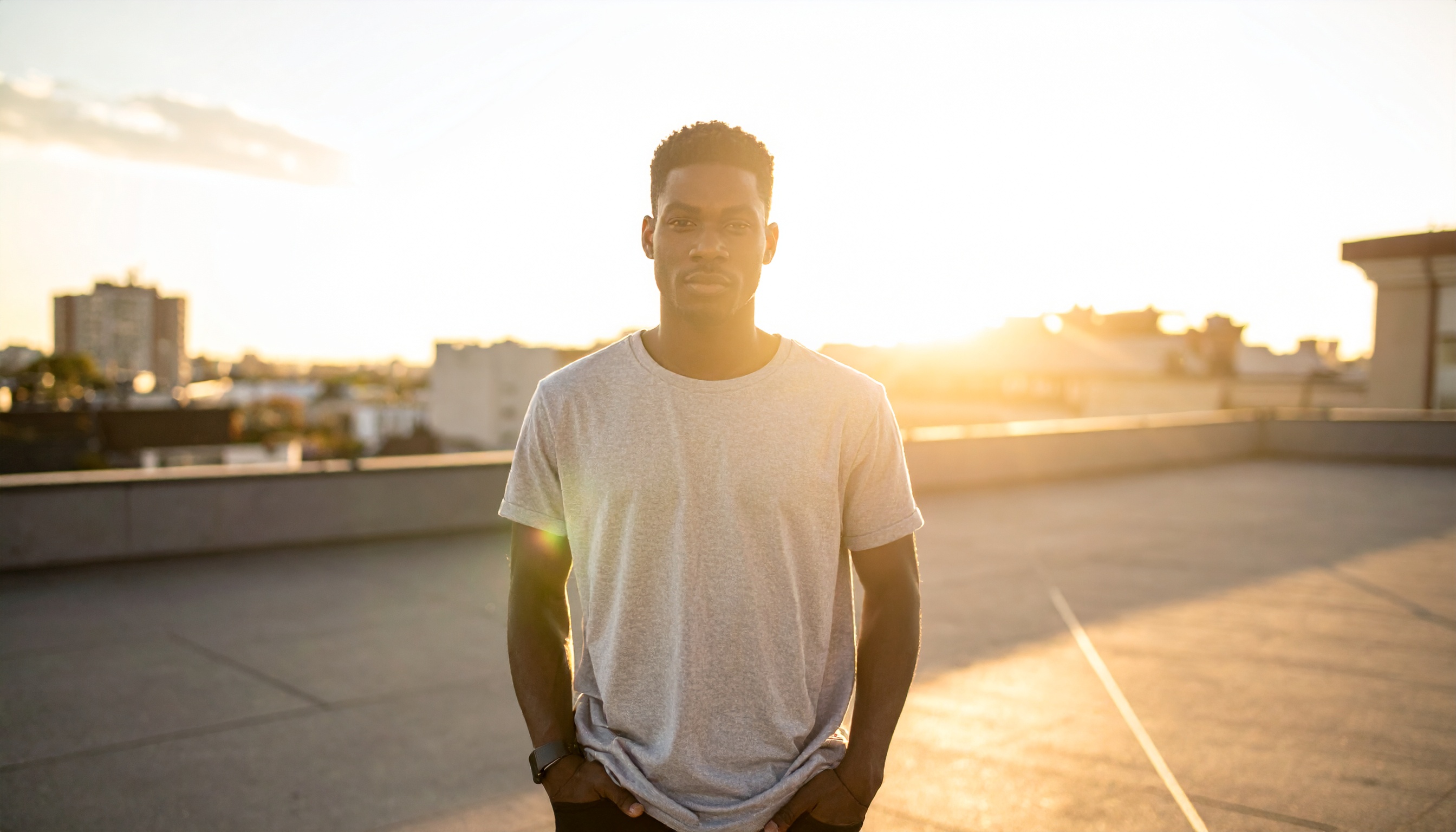 This image shows a man standing on a rooftop during sunset, bathed in warm, golden light
