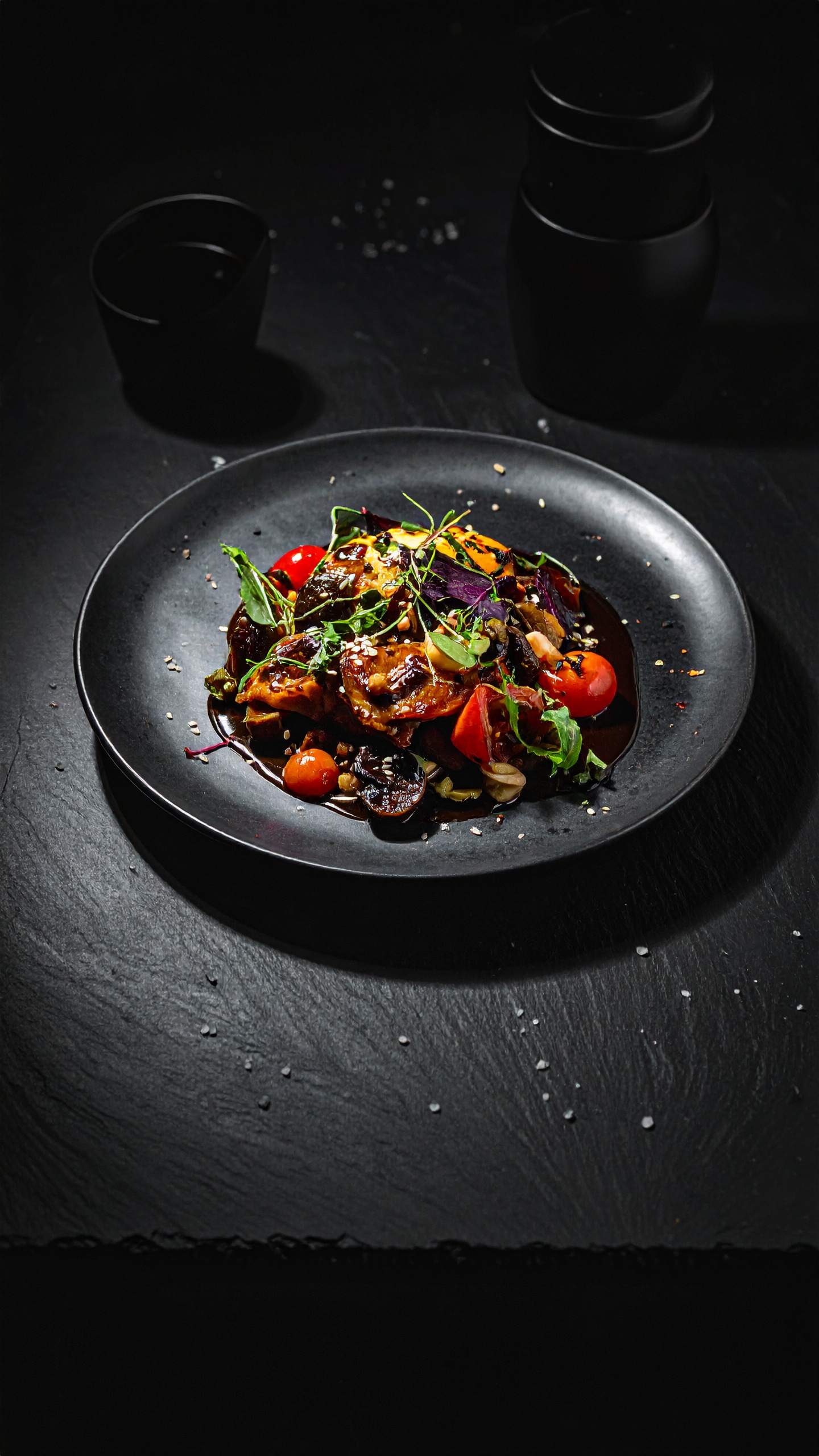 A vibrant roasted vegetable salad is elegantly presented on a sleek black plate