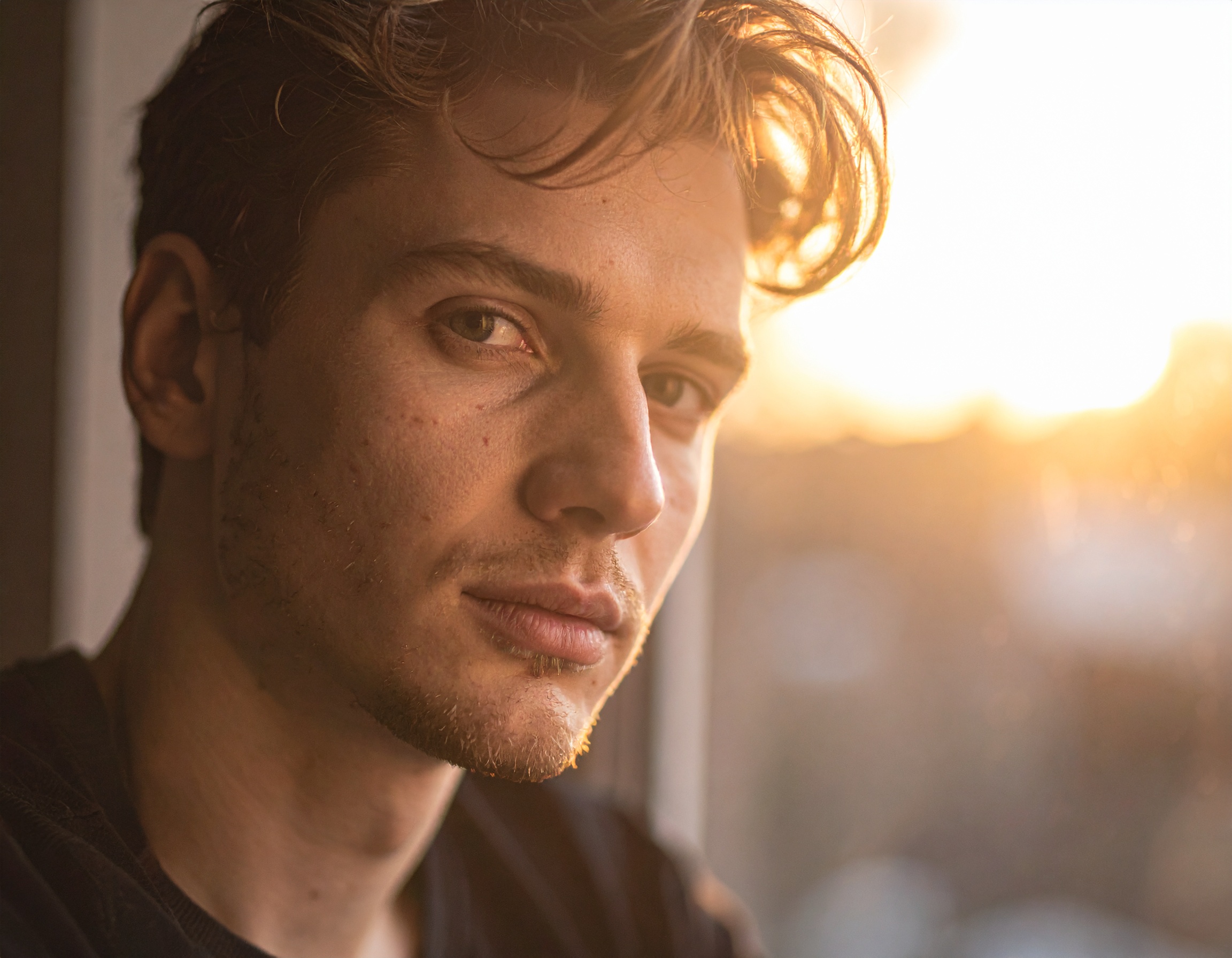 A contemplative man gazes out of a window at sunset, bathed in warm golden light