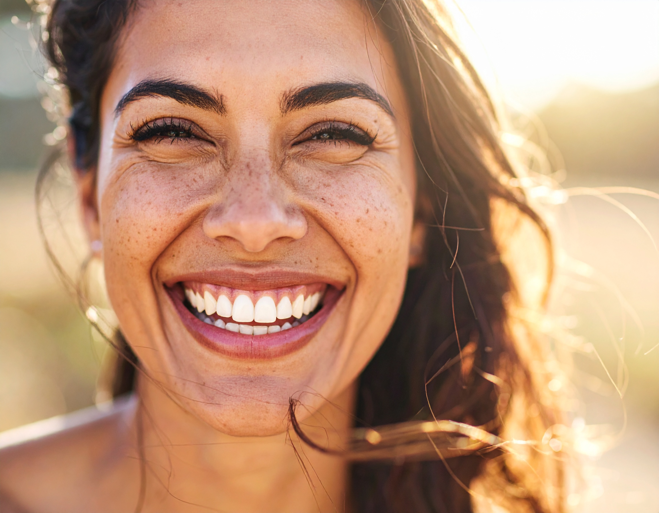 A woman with a radiant smile is illuminated by sunlight, emphasizing her joyful expression