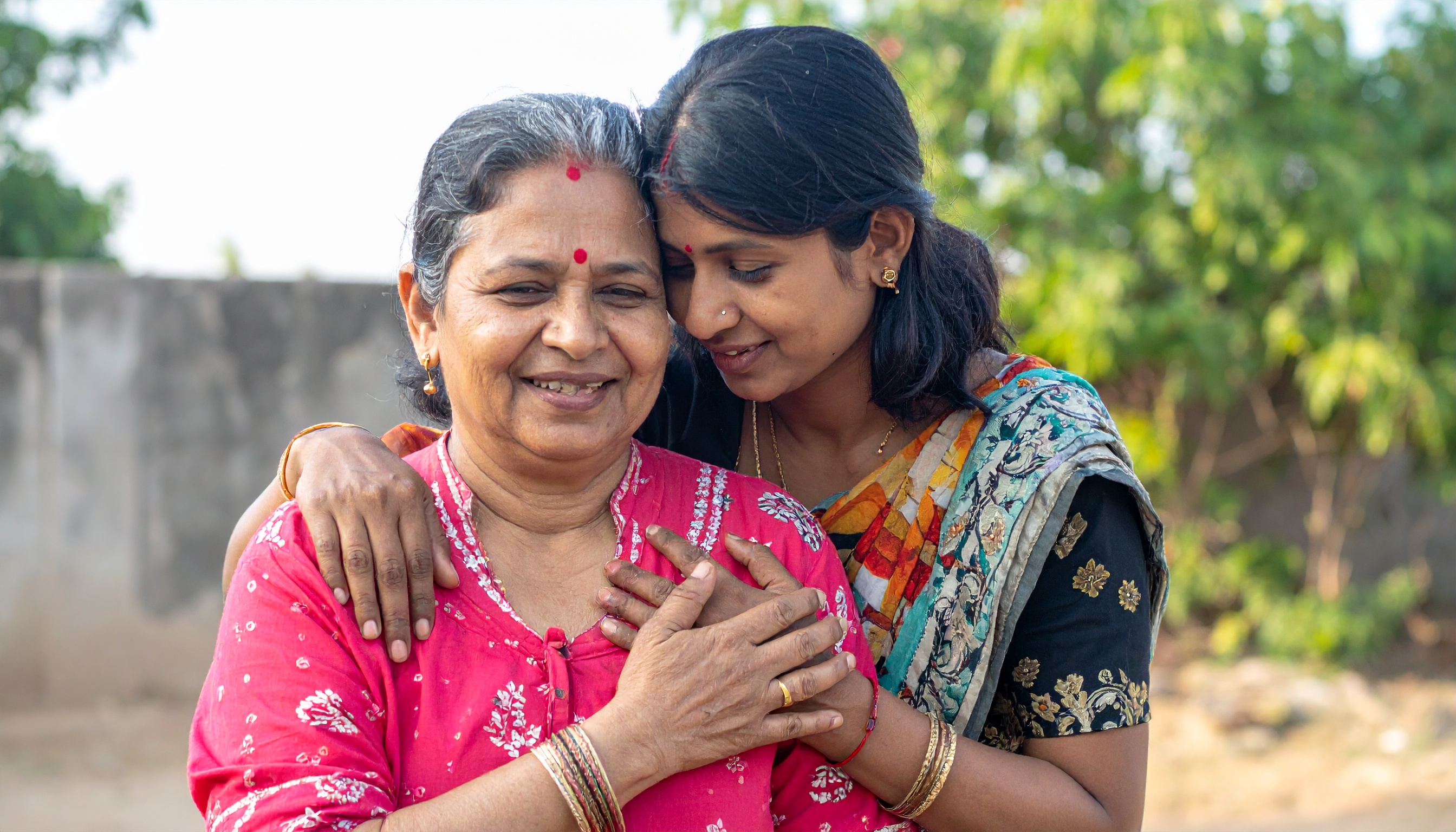 A mother and daughter share a warm, loving embrace outdoors