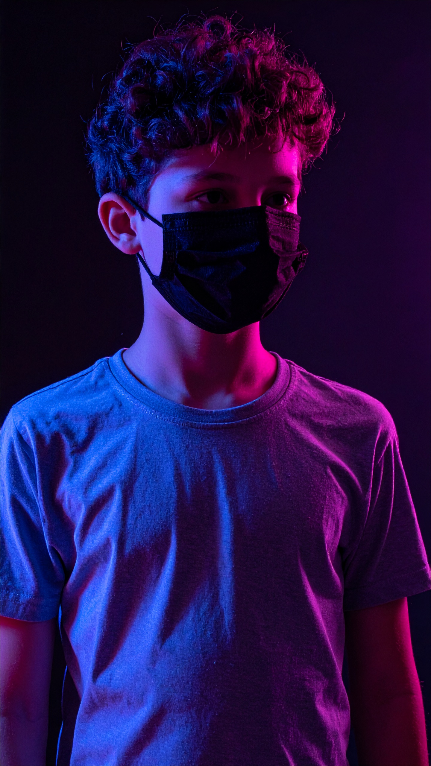 A young person wears a black face mask under dramatic blue and pink lighting