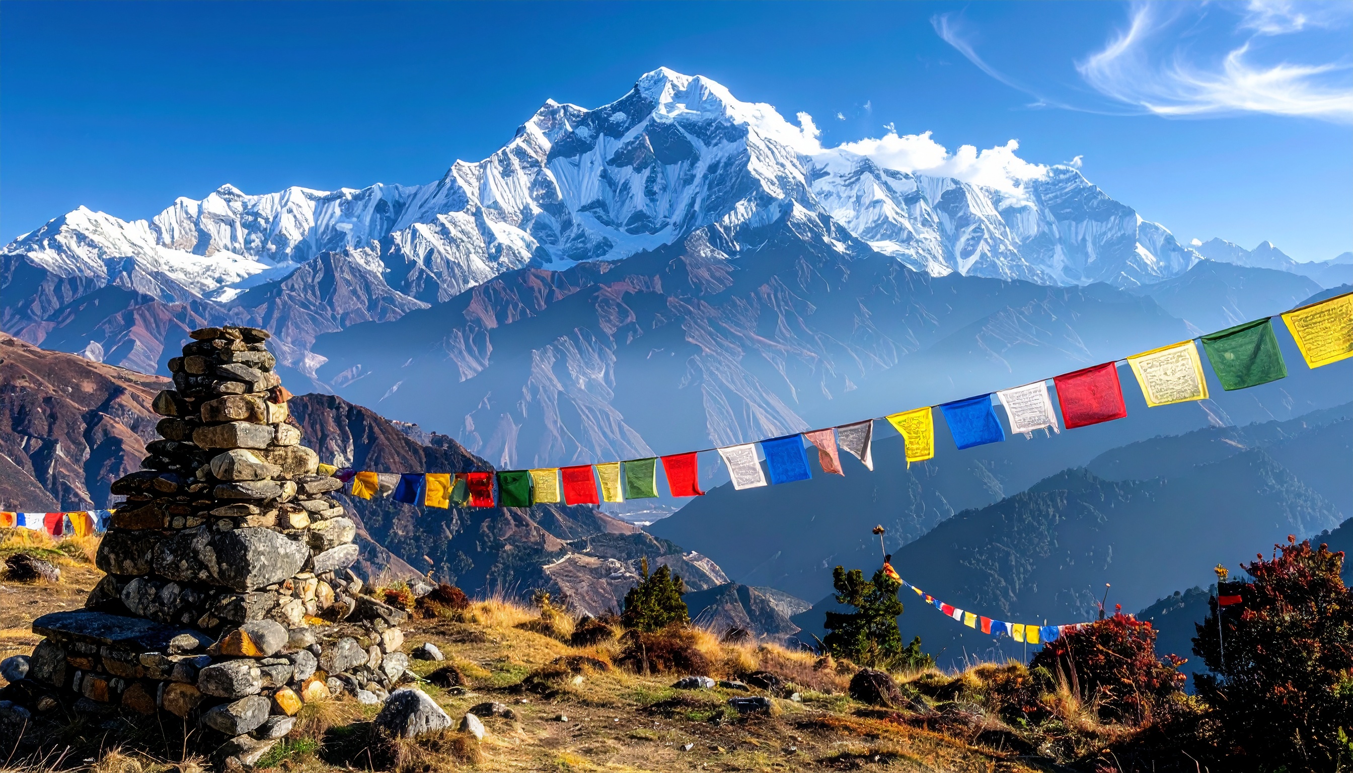 Montanhas majestosas cobertas de neve são emolduradas por uma fileira de bandeiras de oração coloridas que flutuam ao vento. Esses elementos simbolizam paz e espiritualidade, comuns em regiões como o Himalaia. O contraste entre as pedras empilhadas e as cores vibrantes das bandeiras cria uma cena visualmente impactante e harmônica. Ideal para uso em decoração de ambientes que buscam inspirar tranquilidade e contemplação. As bandeiras de oração adicionam um toque cultural e espiritual, tornando a imagem especialmente relevante para temas relacionados à meditação e viagens espirituais.