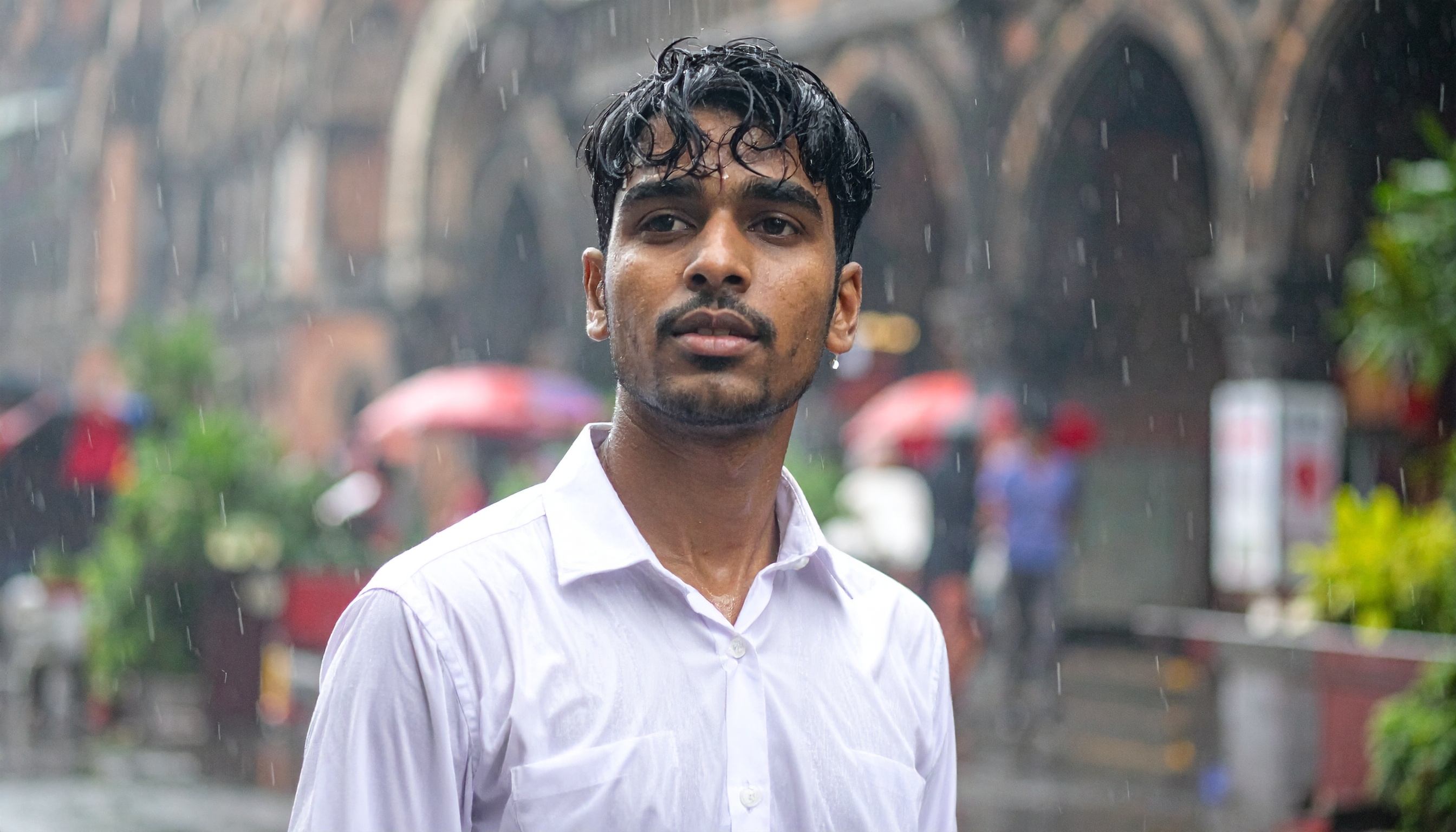 A young man stands in the rain on a bustling city street