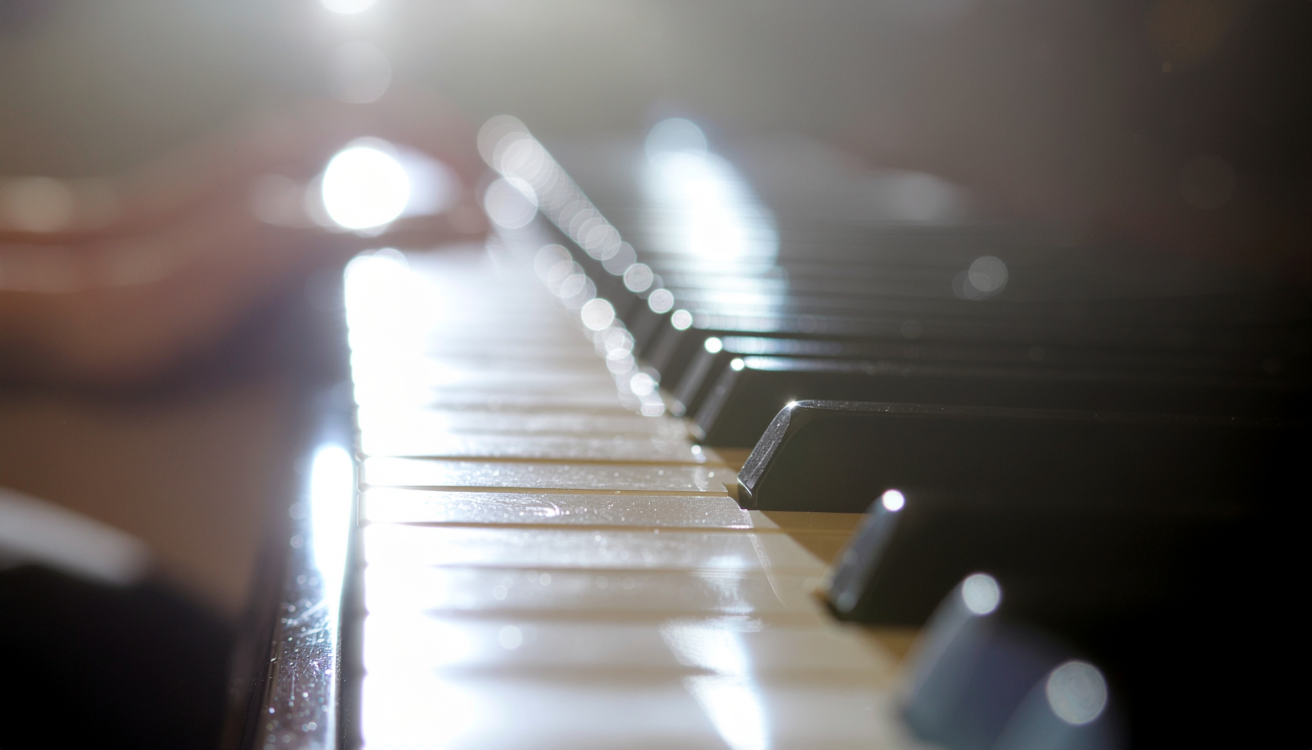 Teclas de piano em close com luz suave refletindo na superfície, criando um efeito bokeh. A composição destaca as teclas brancas e pretas em perspectiva, oferecendo um sentimento de serenidade e foco. A iluminação natural entra pelo lado esquerdo, acentuando a textura do teclado com um efeito estético sofisticado.