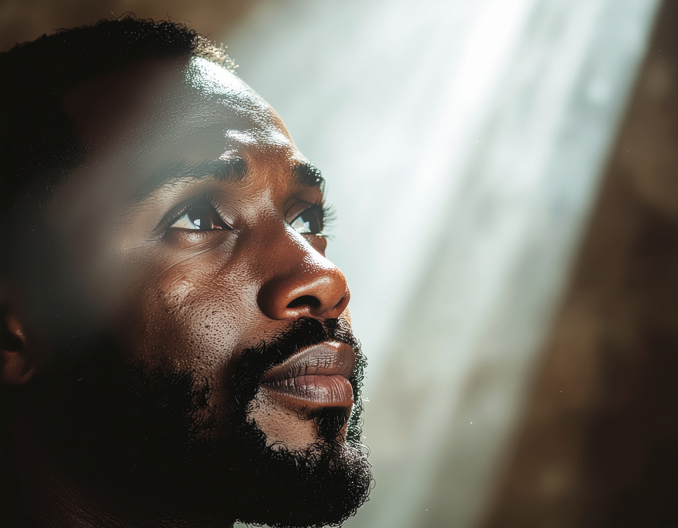 Homem olhando para cima com expressão contemplativa em um ambiente iluminado por feixe de luz suave, transmitindo esperança e introspecção, com foco em detalhes faciais realistas.