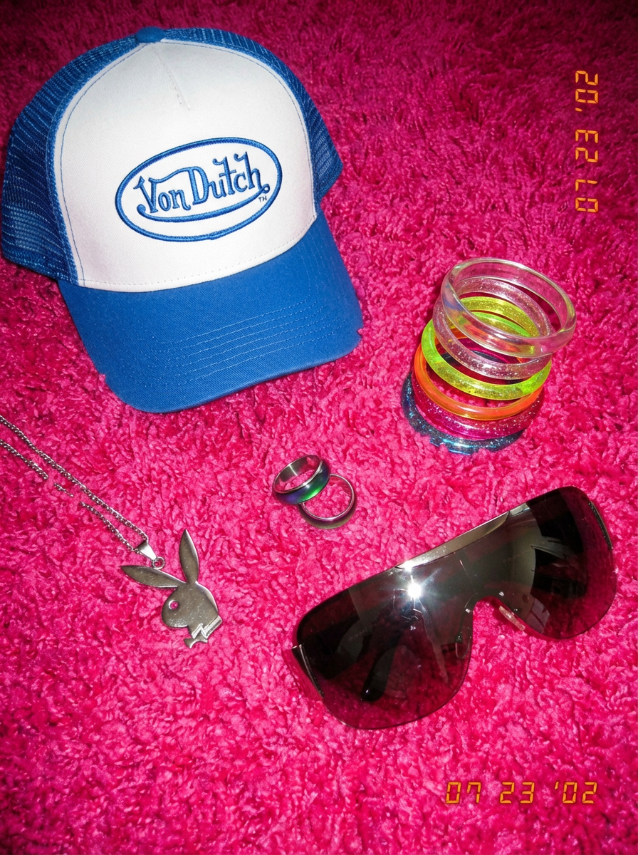 A stylish Von Dutch cap rests on a vibrant pink carpet alongside a mix of trendy accessories