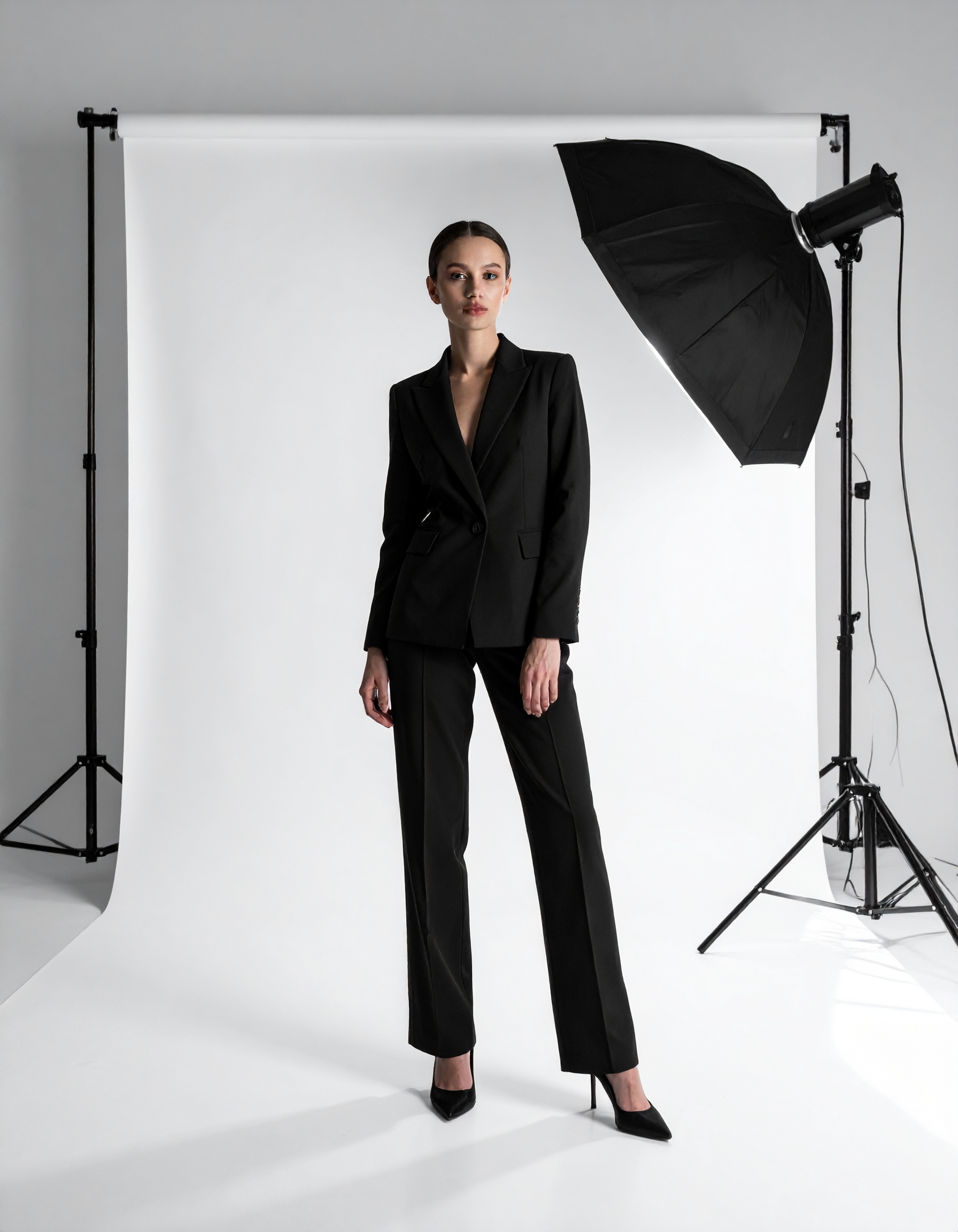 A professional model poses confidently in a sleek black business suit against a clean studio