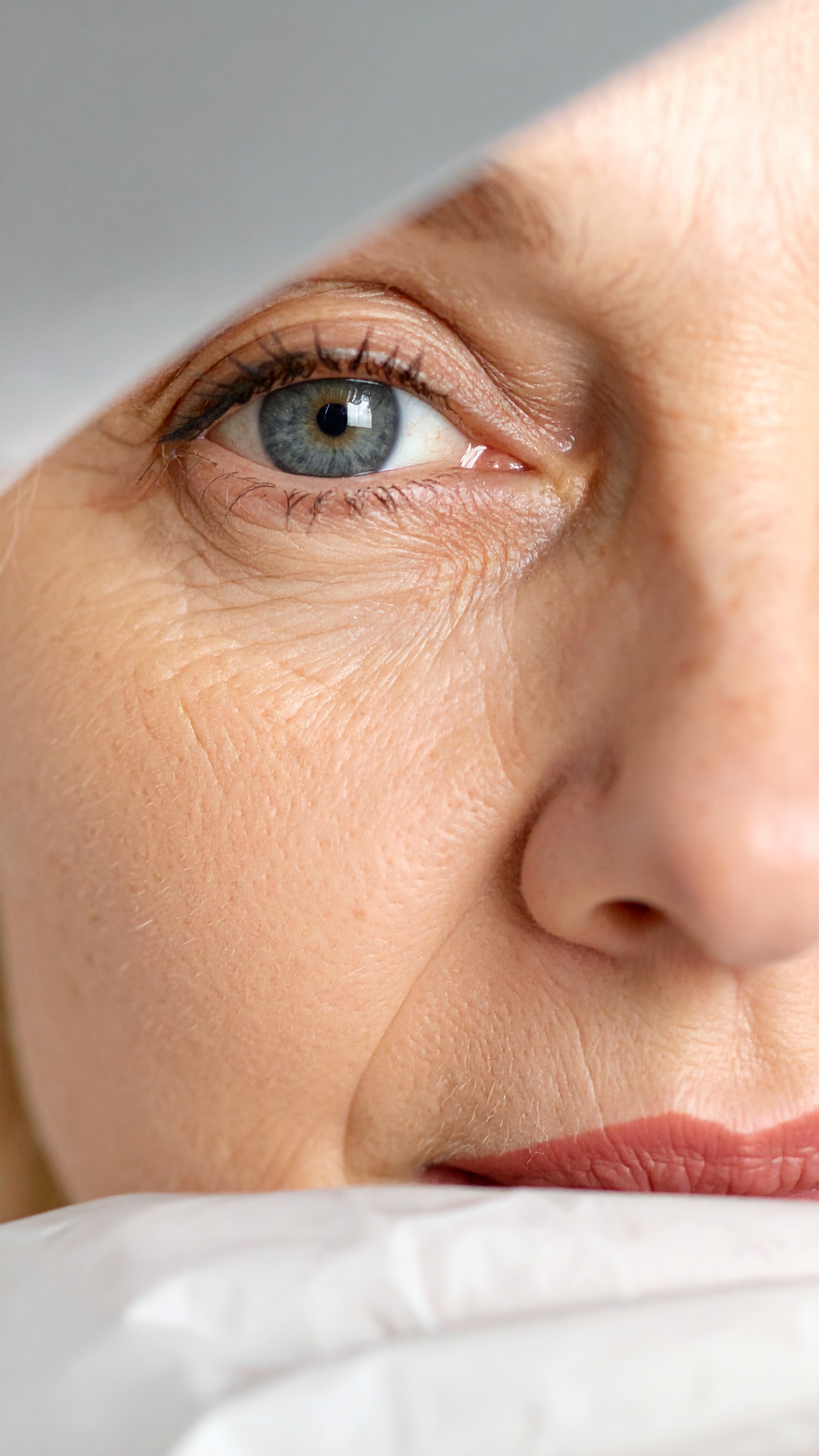 A close-up of a mature woman's eye reveals fine lines and a hint of makeup