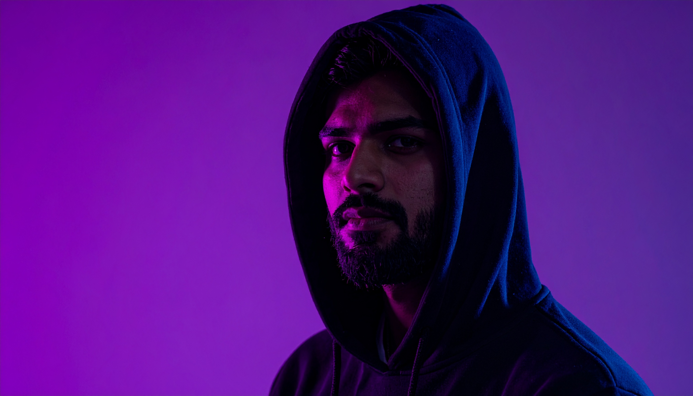 A person in a hooded sweatshirt is illuminated by vibrant purple and blue lighting