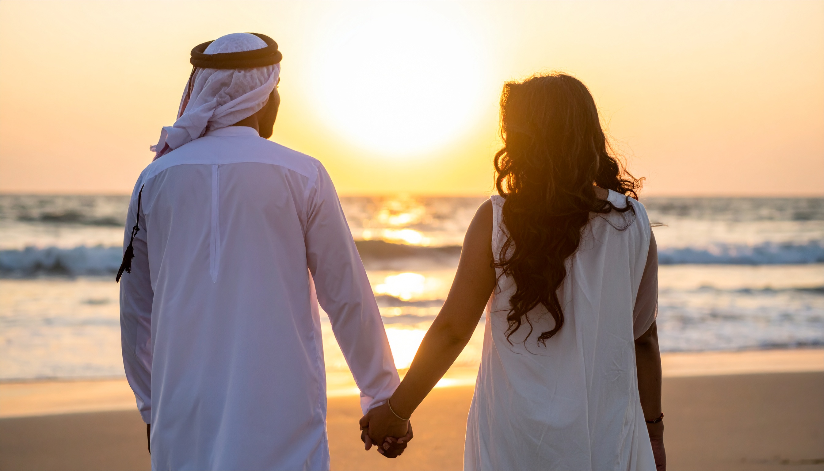A couple holds hands on a serene beach at sunset