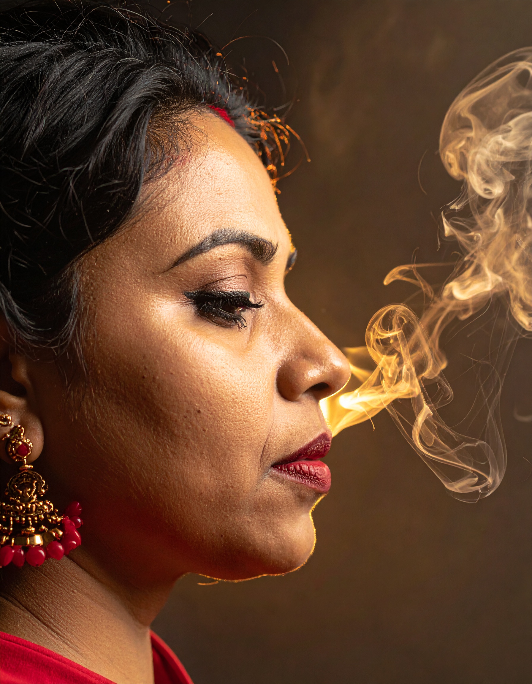 A woman with intricate jewelry exhales a swirl of smoke