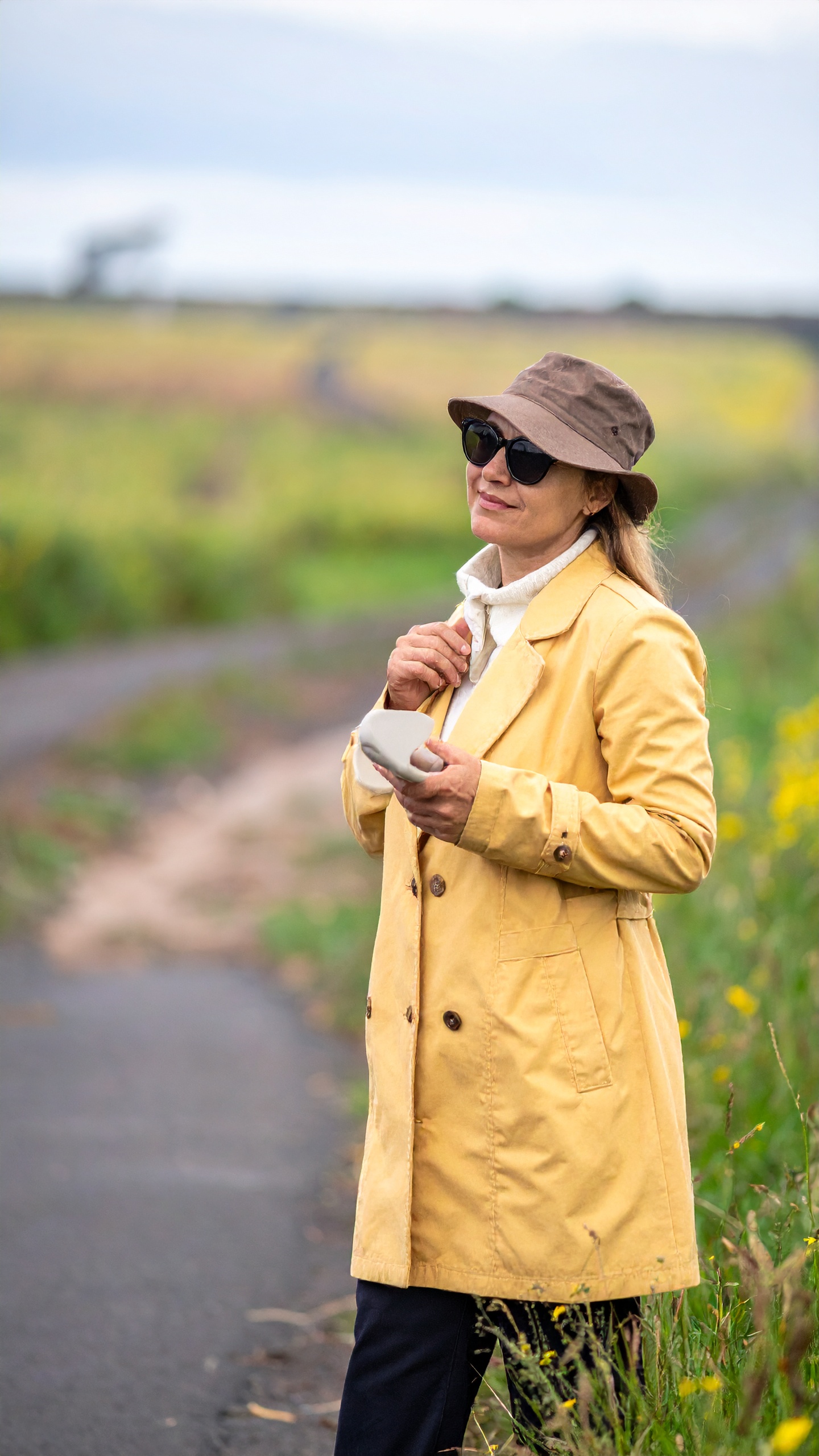 Woman Standing on a Rural Path with Yellow Coat and Brown Hat