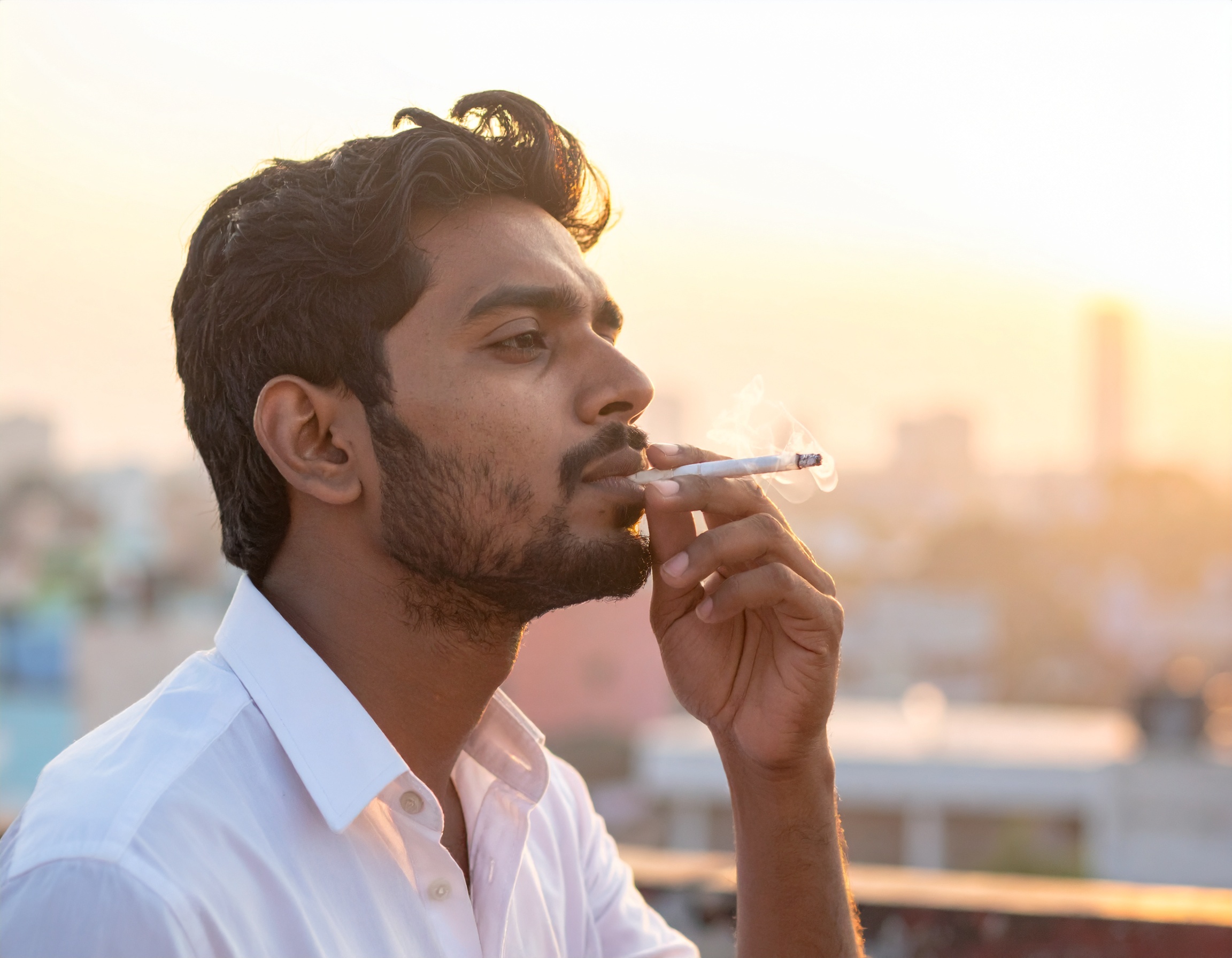 A man is enjoying a cigarette on a rooftop during sunset