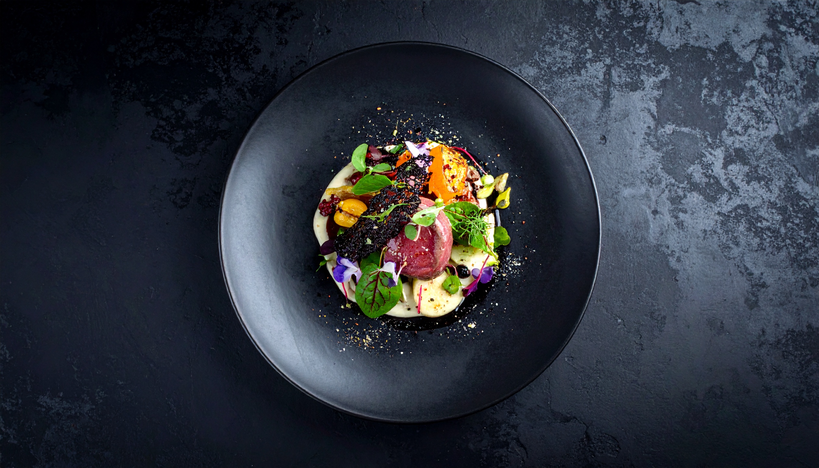 A gourmet dish artfully plated on a textured black surface