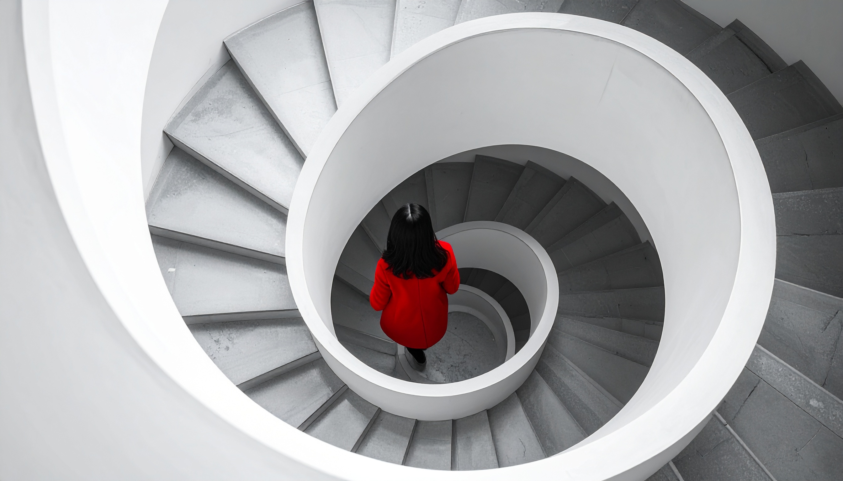 A woman in a vibrant red coat descends a spiral staircase