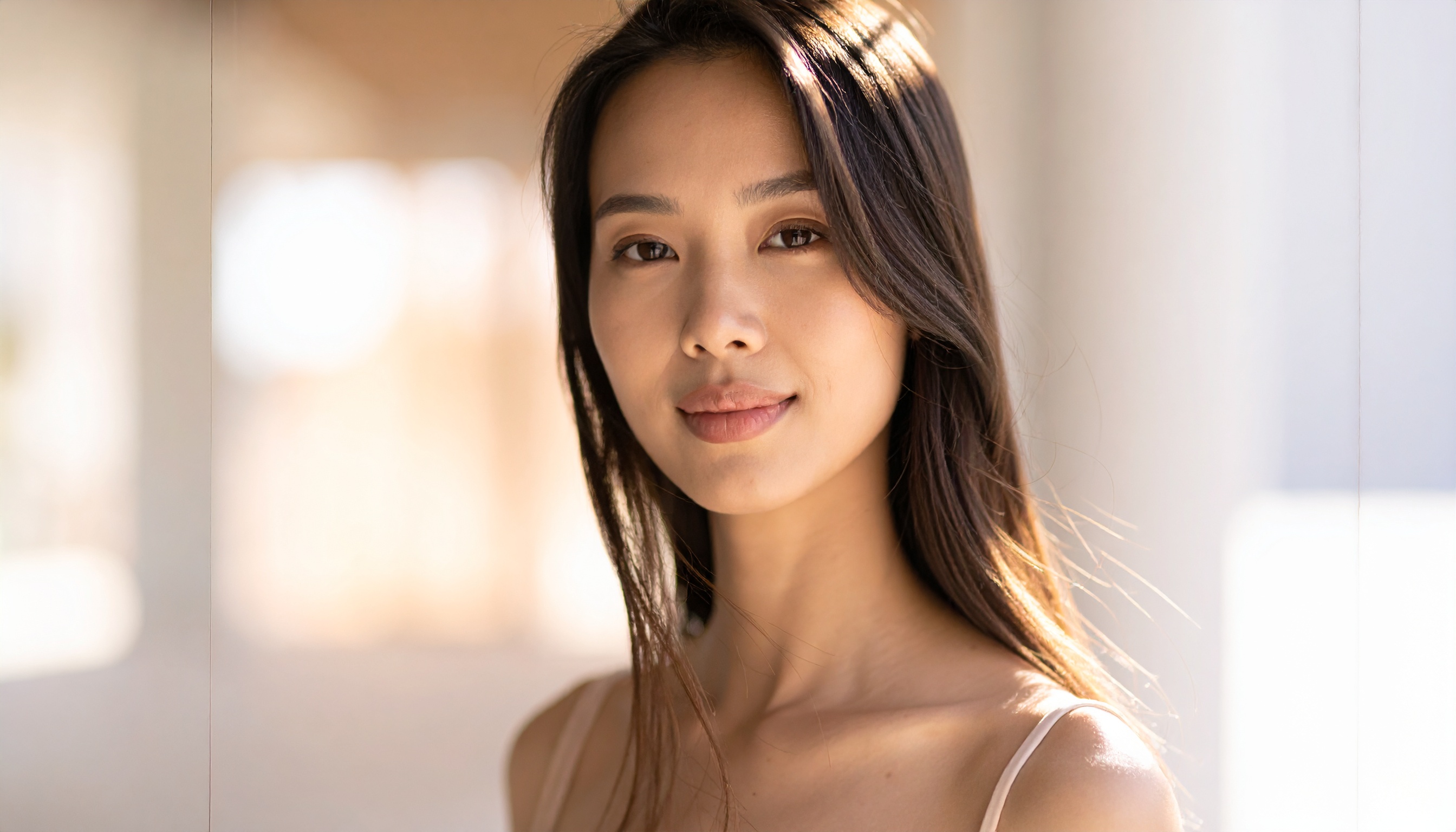 A young woman with long dark hair stands in soft lighting, exuding a sense of calm and poise