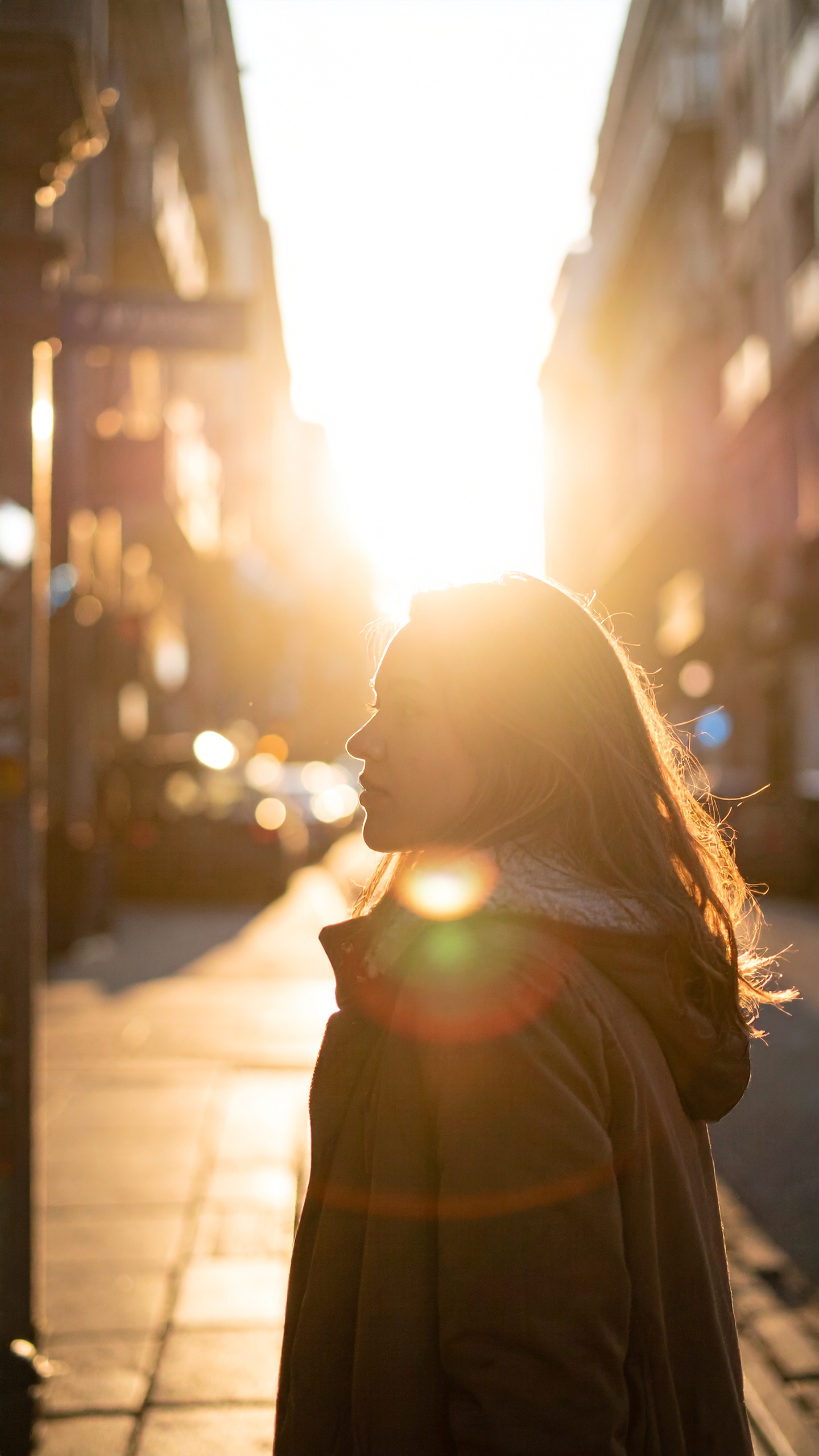 Sunlight silhouettes a person standing on a city street