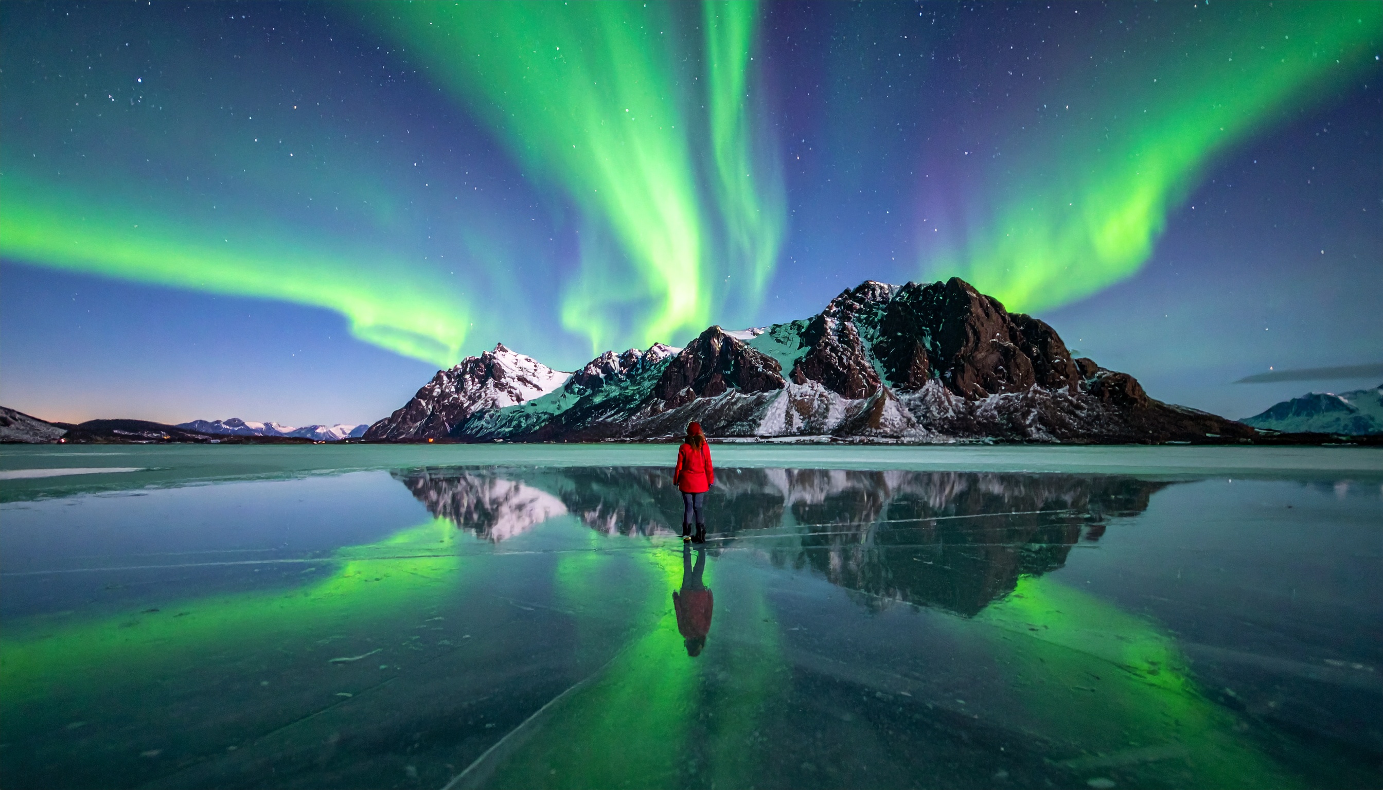 A vivid display of the Northern Lights illuminates the night sky above a frozen lake,