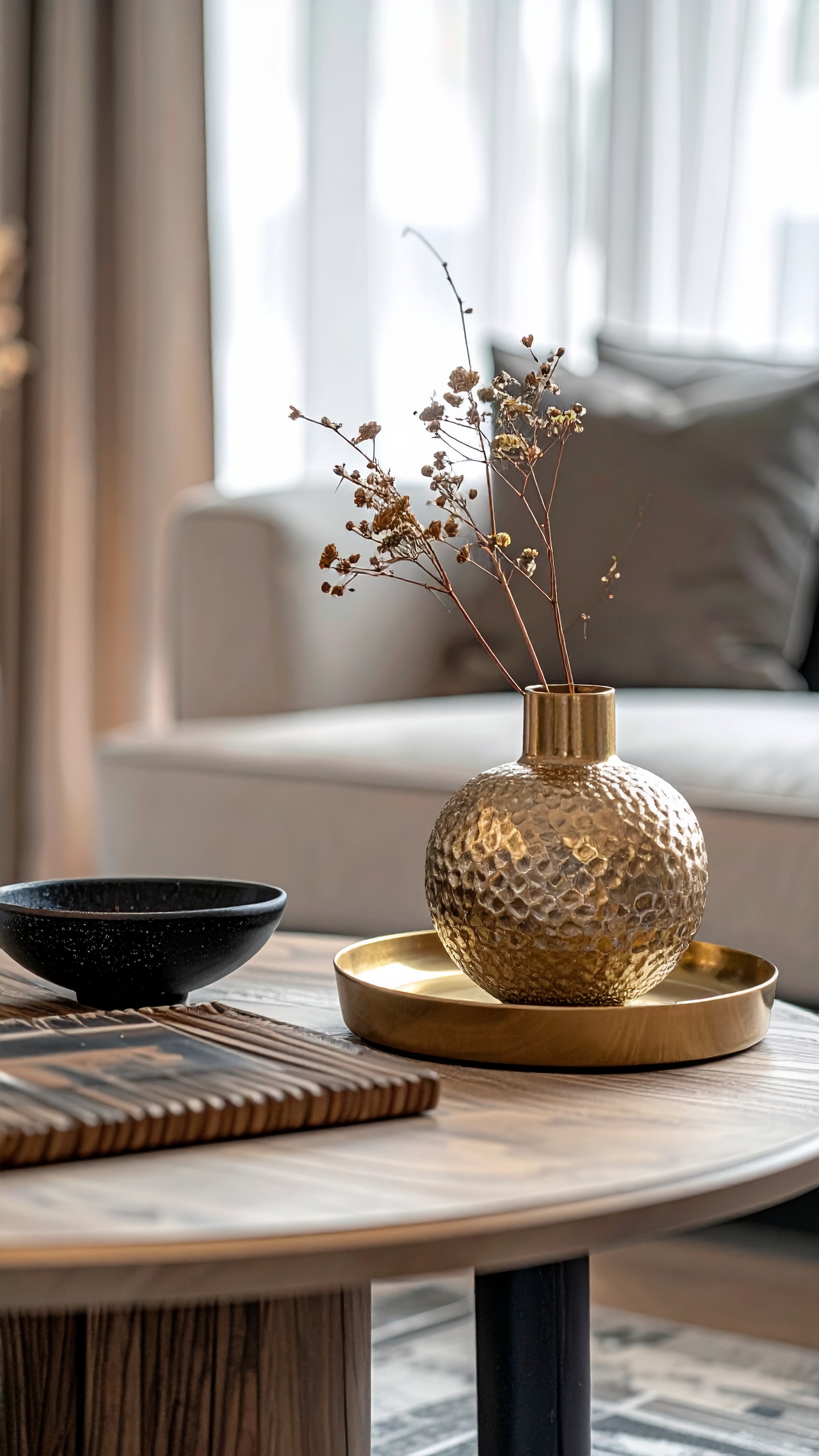 Golden hammered vase with dried flowers on a wooden table adds elegance to a modern living space