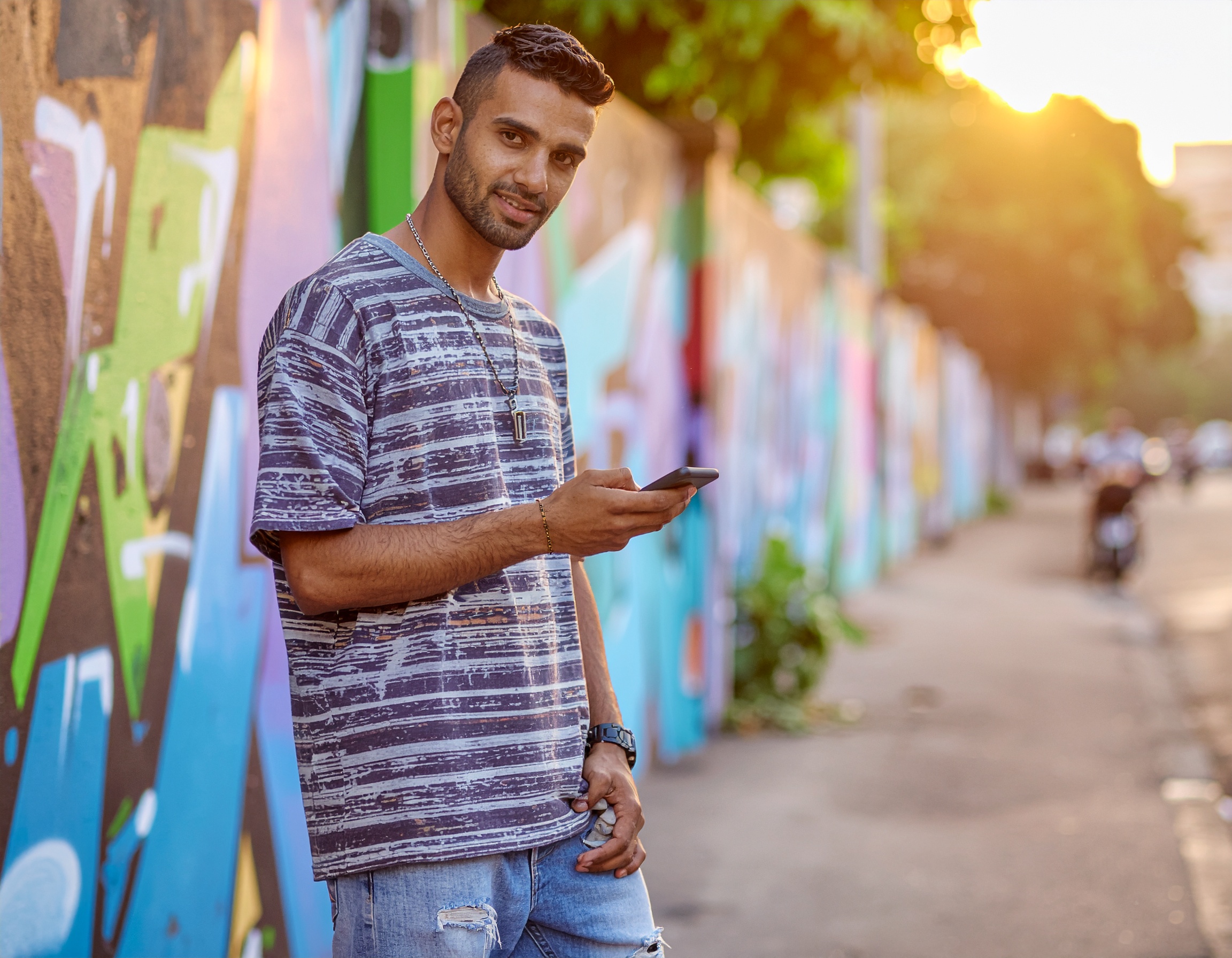 A confident man stands against a colorful urban graffiti wall, engaging with his smartphone