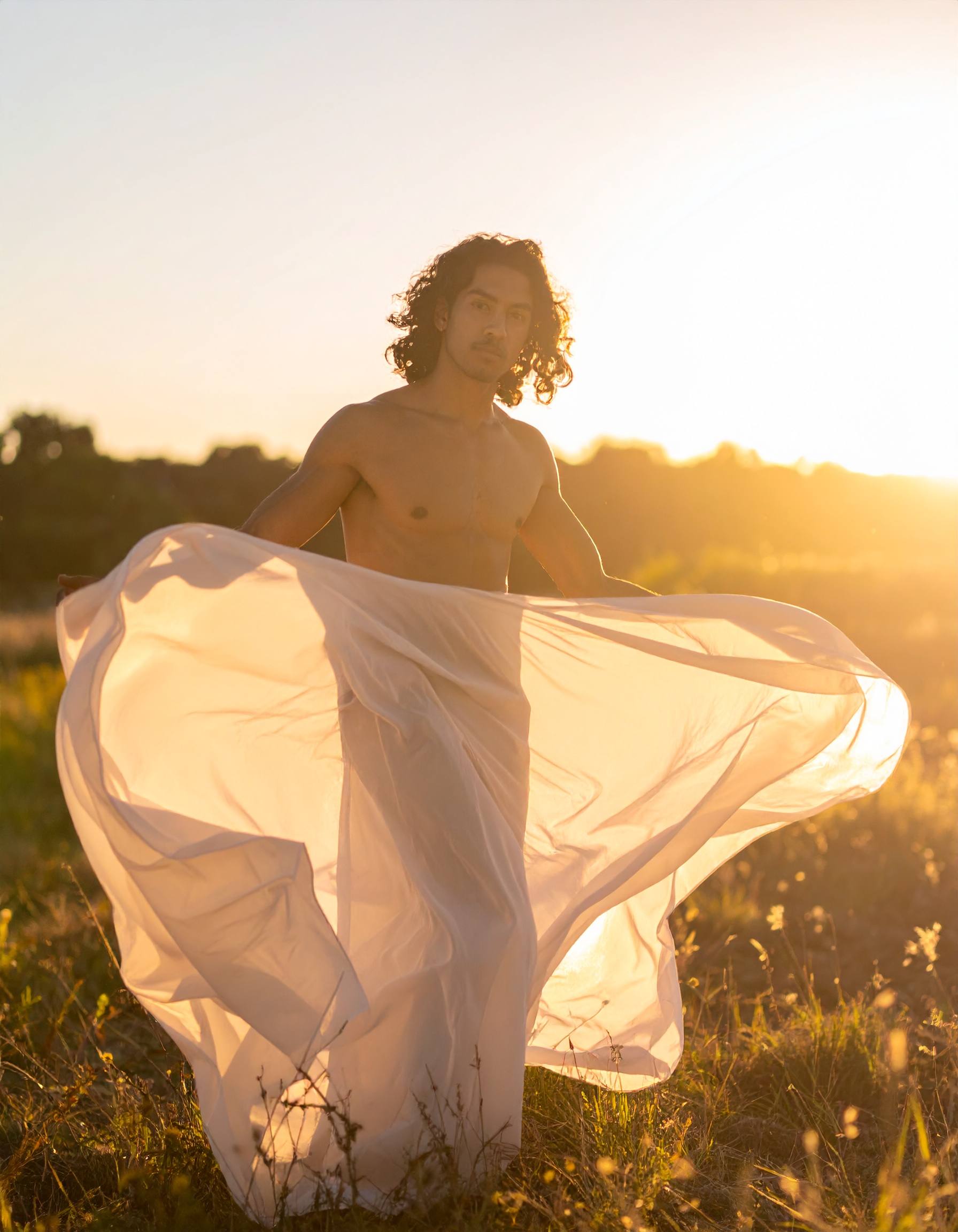 A man stands in a sunlit field holding a flowing white fabric