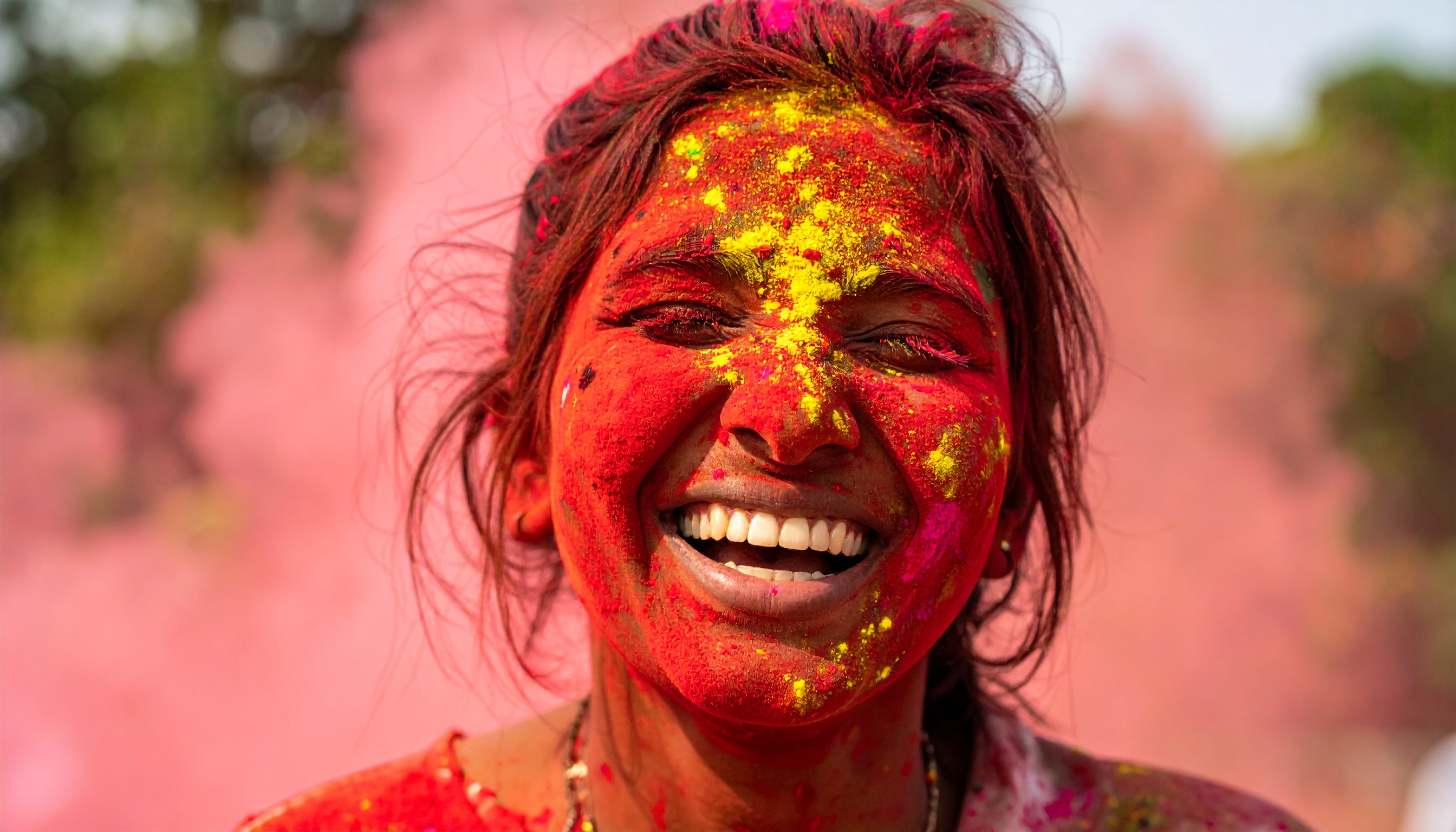 A woman joyfully covered in vibrant colors participates in a festival, exuding happiness