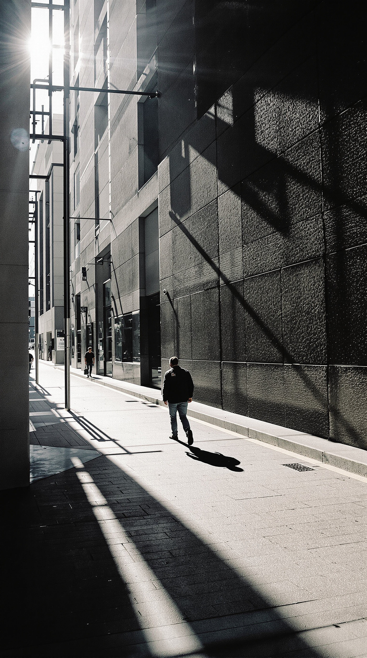 A lone figure walks down a shadowed urban alleyway with tall buildings on either side