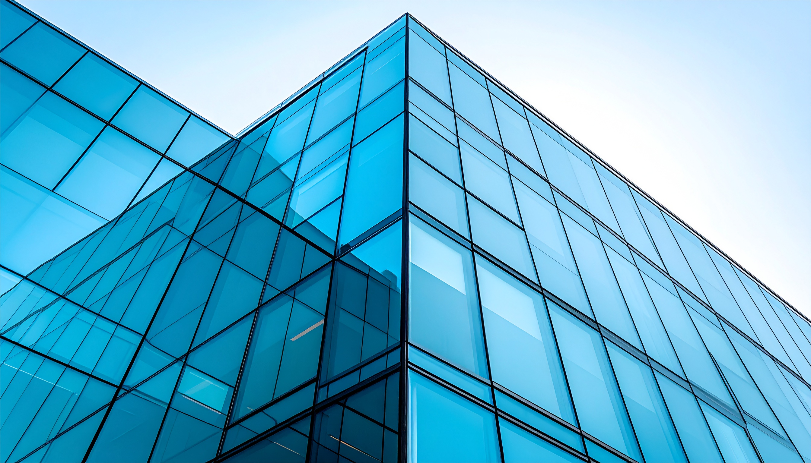 Fachada de edifício moderno com painéis de vidro azul refletindo o céu, ângulo baixo destaca linhas geométricas e perspectiva, iluminação natural realça a transparência e a arquitetura minimalista.