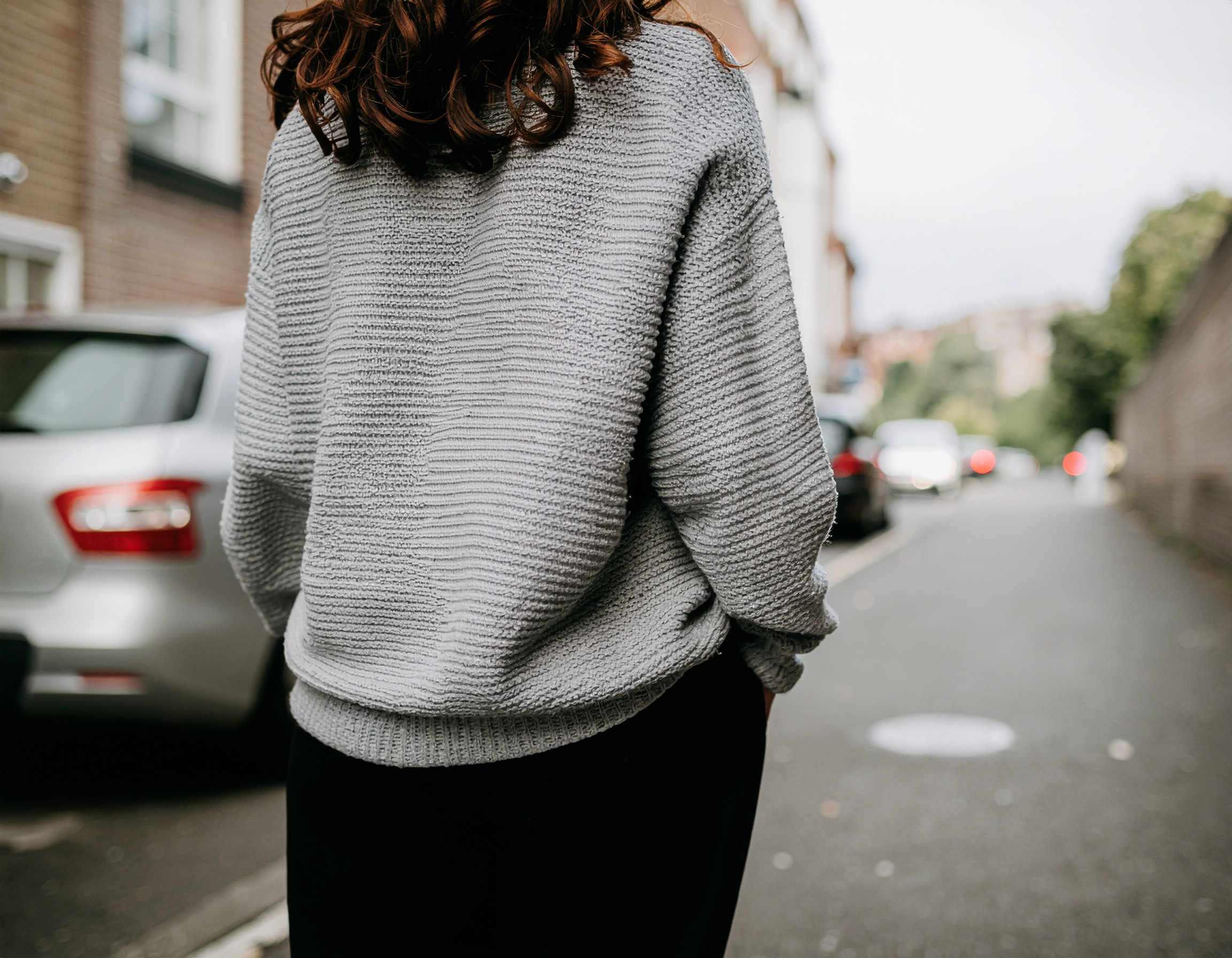 Casaco cinza texturizado visto de costas em ambiente urbano. Ideal para dias amenos, oferece conforto e estilo casual. A textura do tecido é destacada, combinando bem com calças escuras. Perfeito para passeios ao ar livre ou encontros casuais. Adiciona um toque de sofisticação ao look do dia a dia.