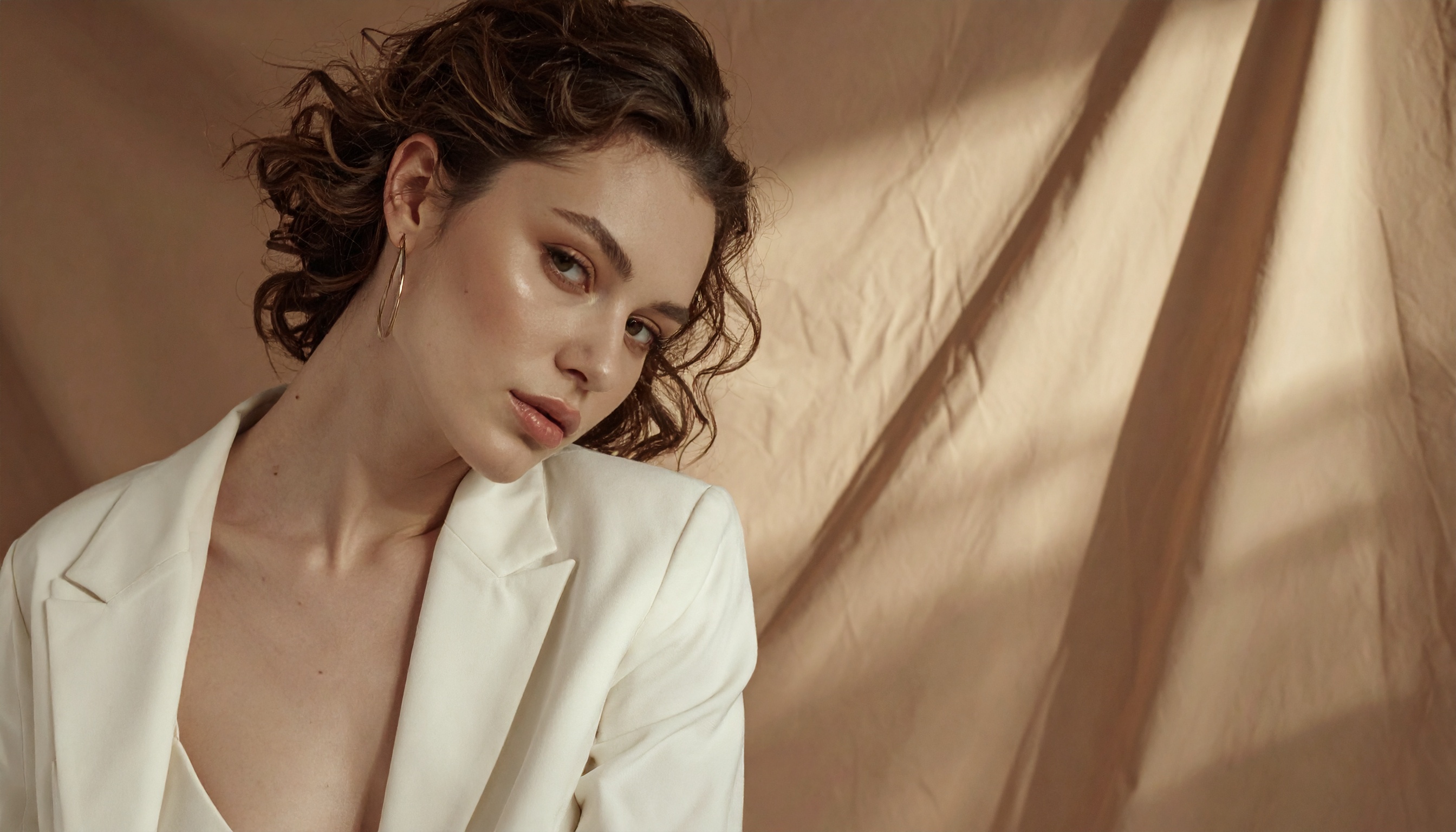 Mulher com expressão contemplativa veste blazer branco elegante. Ideal para campanhas de moda que buscam destacar sofisticação e estilo. A luz suave e o fundo neutro realçam a delicadeza das feições e o tom da pele. Ótima escolha para editoriais de moda, catálogos de roupas e redes sociais que promovem elegância. A imagem transmite uma sensação de modernidade e simplicidade refinada.